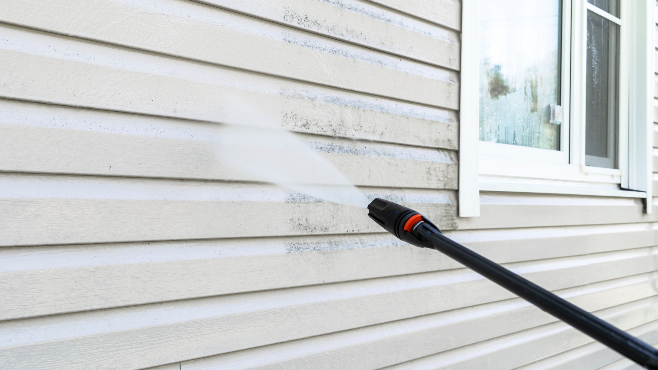 close up view of power washing nozzle spraying the side of a home